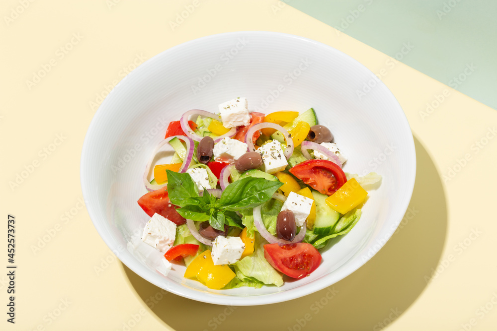 Greek salad in white plate hard shadows on blue and yellow