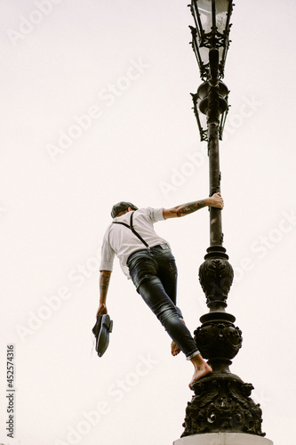 Young bearded tattooed man. A romantic guy in a white shirt, cap and suspenders walks in the city. revolves around a lamppost. Peaky Blinders. old-fashioned, retro.