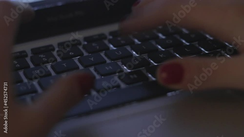 An HD footage of female hands with painted fingernails typing in a laptop keyboard photo