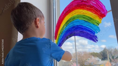 Child drawing a rainbow on a glass of a window at home.  photo