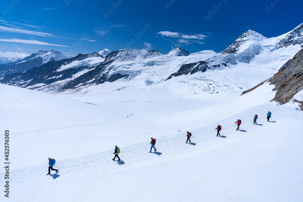 des randonneurs en file indienne dans la neige au milieu d'un paysage de montagnes alpestres