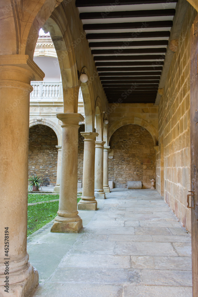Backyard of medieval monastery with arch and column. Catholic abbey. Church courtyard on Camino de Santiago. Religious architecture. Empty outdoor corridor in cathedral. Old cloister yard.