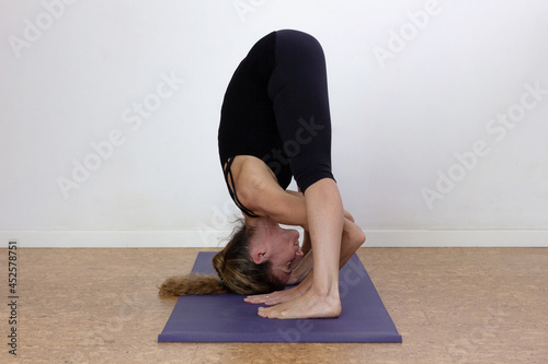 Female yogi in prasarita padottanasana over white background. Fit woman practicing wide legged forward bend yoga pose indoors. Hands and feet on floor. Flexibility, workout, exercise concepts photo