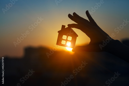 Man holding  wooden house model against sunset light for sale or rent, family home and shelter concept, real estate, solar energy and eco accommodation