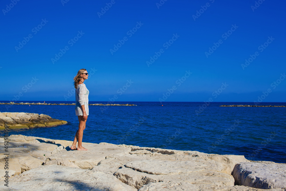 A beautiful girl stands on the rocky shore of the Mediterranean Sea Cyprus.Cheerful girl rests on the sea