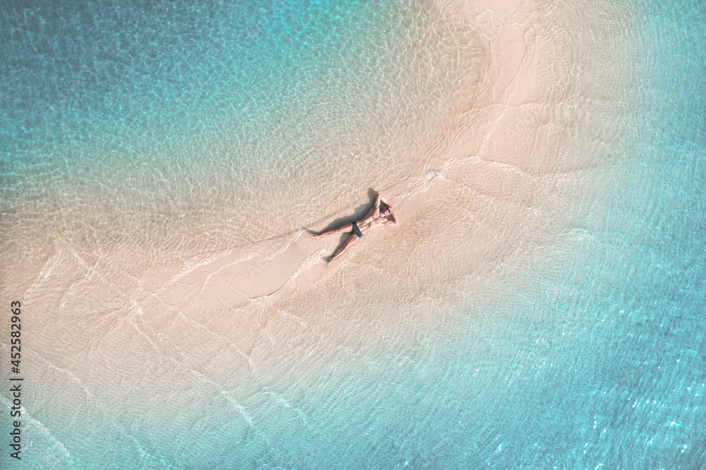 An athletic young man sunbathes on a sandbank in a beautiful azure sea