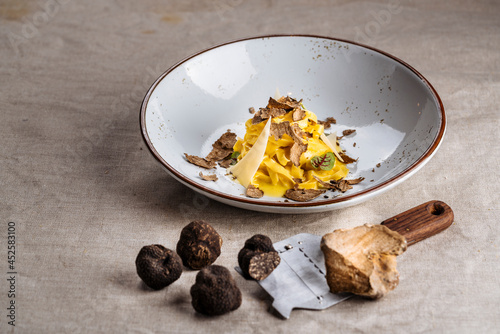 Delicious Italian Tagliatelle or Fettuccine pasta with shaved parmesan cheese and truffle mushroom. Black Truffle and White Truffle with shaver as foreground over rustic fabric cloth. Warm earth tone. photo