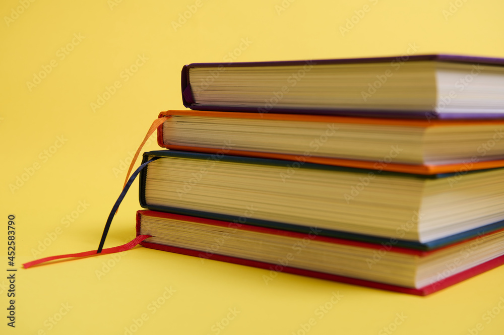 Close-up studio shot of a stack of multicolored books on yellow surface background with copy space for text. Teacher's Day concept, Knowledge, literature ,reading, erudition Close-up studio shot of a stack of multicolored books on yellow surface background with copy space for text. Teacher's Day concept, Knowledge, literature ,reading, erudition