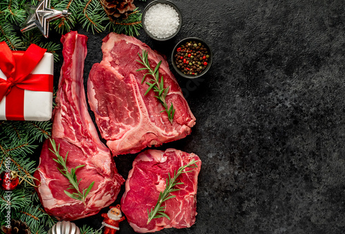 Variety of Christmas Raw Beef Steaks. Ribeye steak, tomahawk, T-bone, with tree and Christmas toys on the stone background with copy space for your text