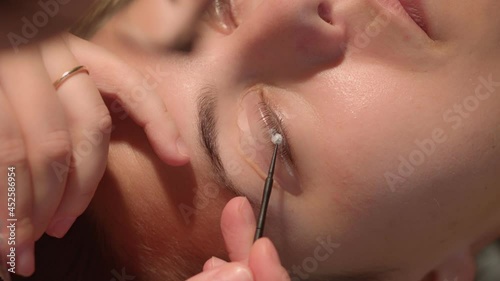 Cosmetic procedure of eye lashes lamination to brunette girl. Beautician master hands at work putting fixing product on eye lashes. Extreme closeup high quality video footage.  photo