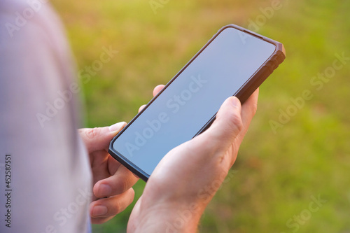 Smartphone in the hands of a man on the street in the park. Man using his cell phone