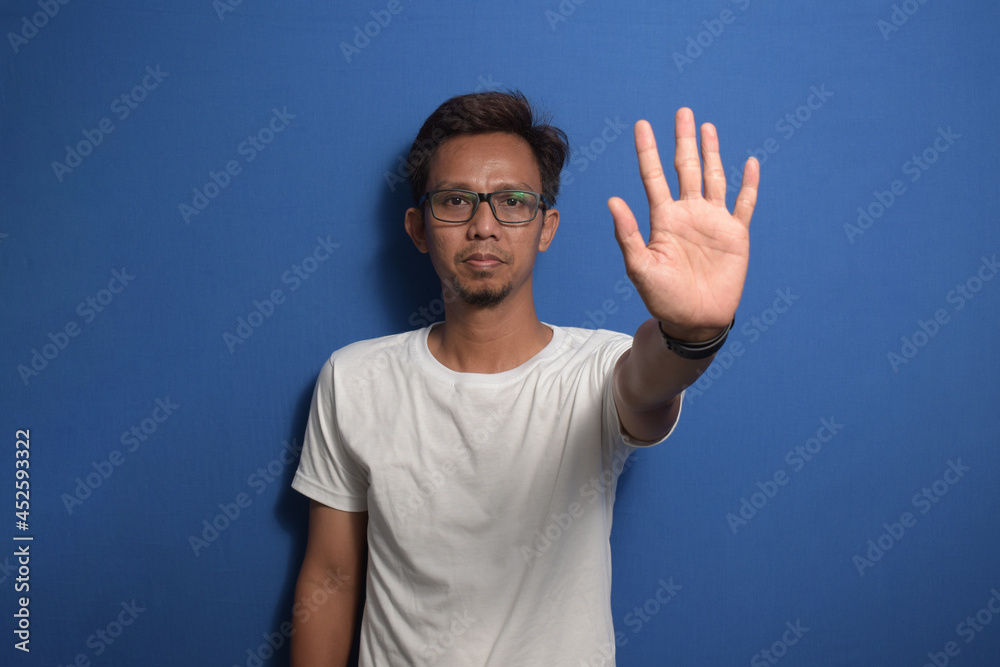 Naklejka premium Young Asian man wearing a white t-shirt over blue background doing stop sing with palm of the hand