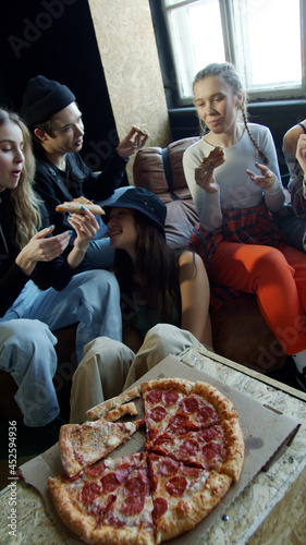 Sporty teenagers with different hairstyles eat pizza sitting on the couch