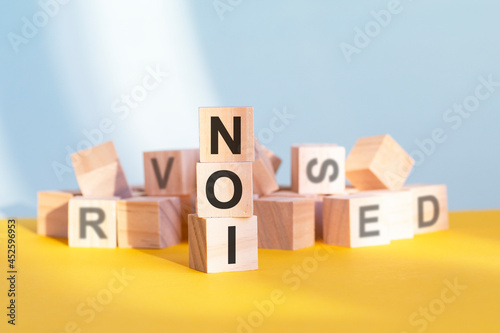 wooden cubes with letters NOI arranged in a vertical pyramid, yellow background