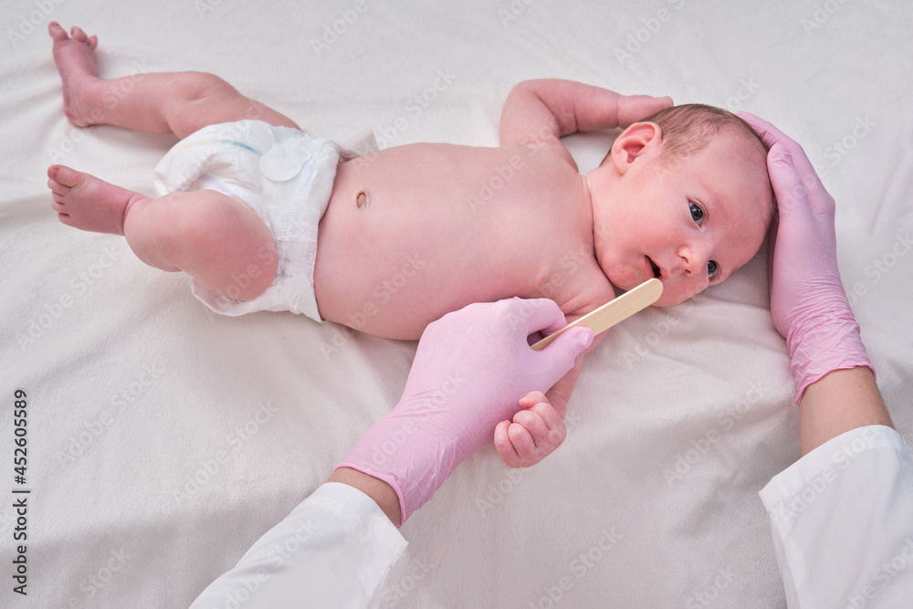 Doctor checks the throat of a newborn child with a plowshare. A nurse in uniform with a wooden stick in her hand examines the child mouth Doctor checks the throat of a newborn child with a plowshare. A nurse in uniform with a wooden stick in her hand examines the child mouth