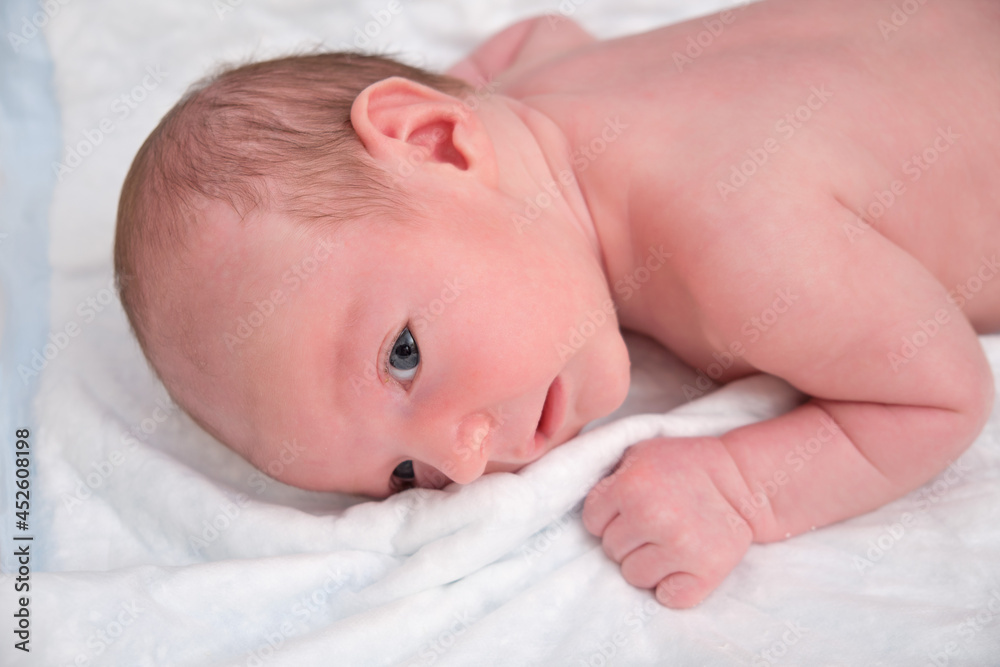 Portrait of a baby boy aged 1 month lying with his eyes open in a crib. Caucasian child in the children bedroom on the bed Portrait of a baby boy aged 1 month lying with his eyes open in a crib. Caucasian child in the children bedroom on the bed