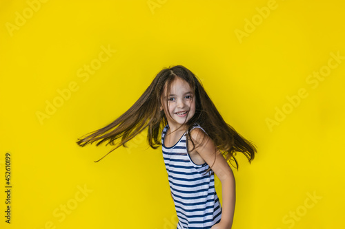 A small smiling girl on a yellow background. She is in a good mood, and she is spinning or dancing.