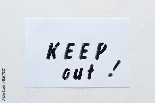 the expression "keep out!" stencilled in black on a white card and placed on a paper background