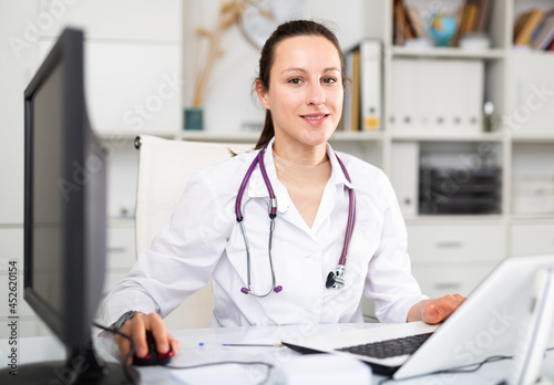 Woman doctor sitting at workplace with computer in her office