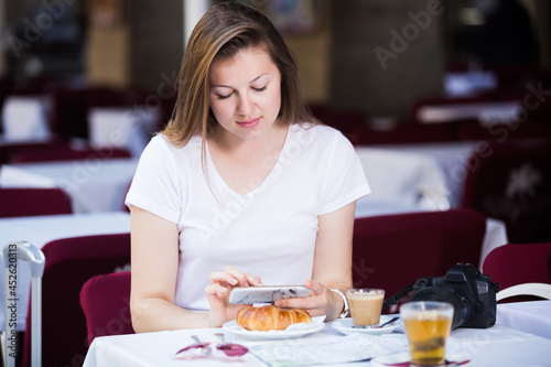 Young cheerful tourist using mobile phone in cafe