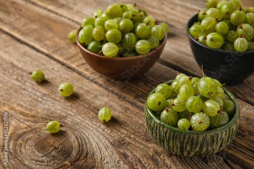 Bowls with fresh ripe gooseberry on wooden background