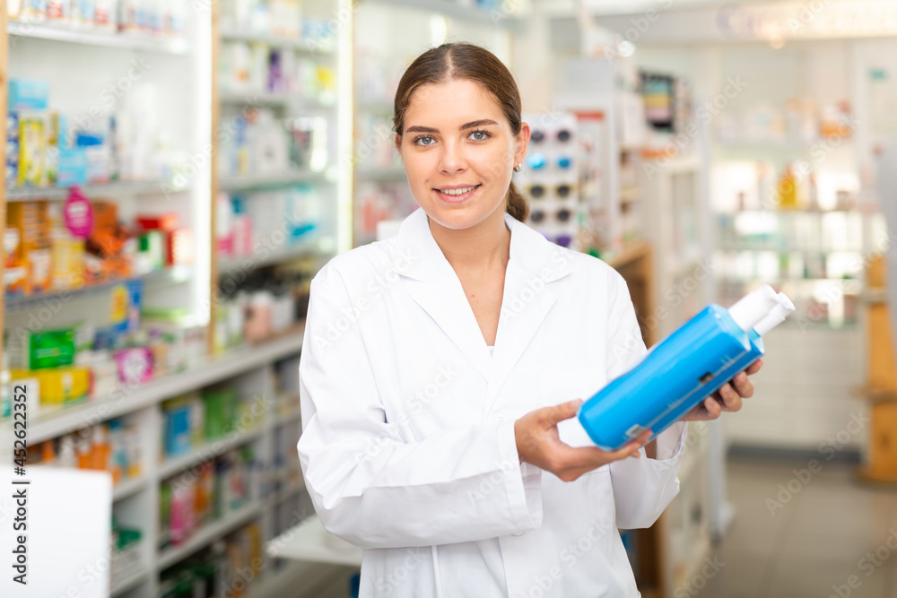 Female pharmacist standing in salesroom of drugstore and demonstrating haircare product