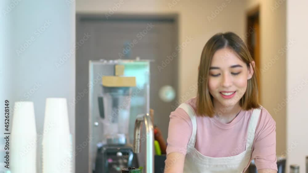 Young beautiful Asian woman coffee shop employee barista working at cafe. Smiling female cashier taking order and serving to customer on counter. Small business owner and part time job working concept Young beautiful Asian woman coffee shop employee barista working at cafe. Smiling female cashier taking order and serving to customer on counter. Small business owner and part time job working concept