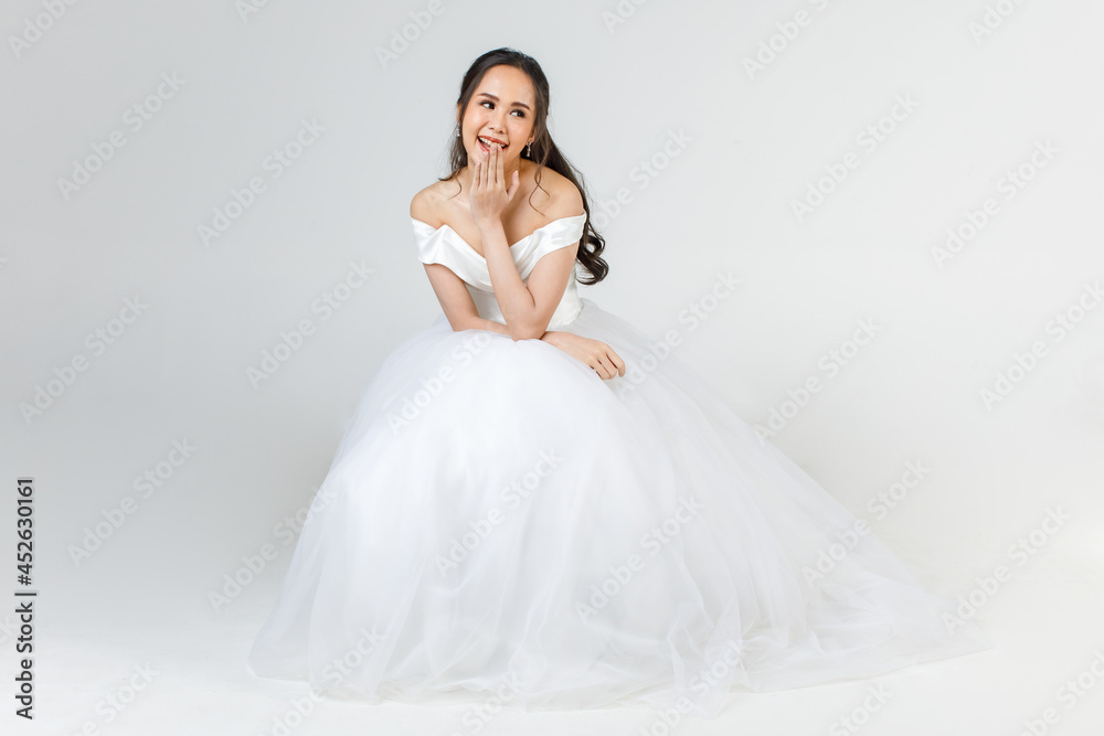 Young attractive Asian woman, soon to be bride, wearing white wedding gown sitting down looking happy. Concept for pre wedding photography Young attractive Asian woman, soon to be bride, wearing white wedding gown sitting down looking happy. Concept for pre wedding photography