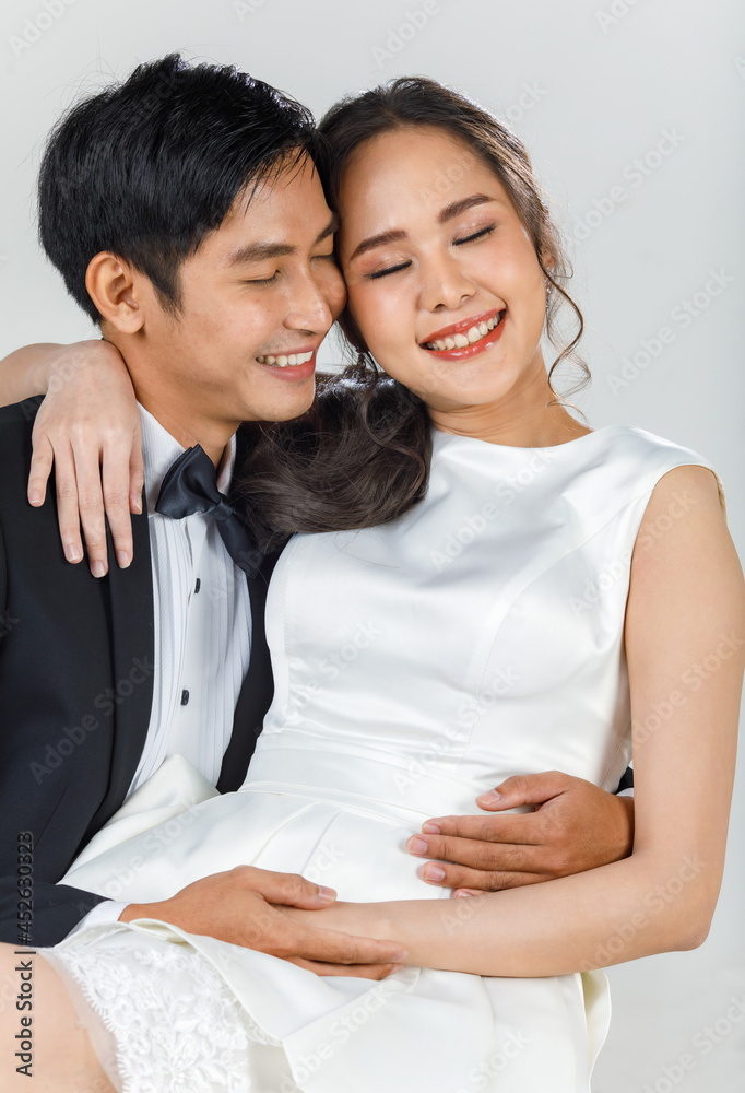 Young attractive Asian couple, bride and groom, woman wearing white wedding dress. Man wearing black tuxedo, hugging each other. Concept for pre wedding photography Young attractive Asian couple, bride and groom, woman wearing white wedding dress. Man wearing black tuxedo, hugging each other. Concept for pre wedding photography