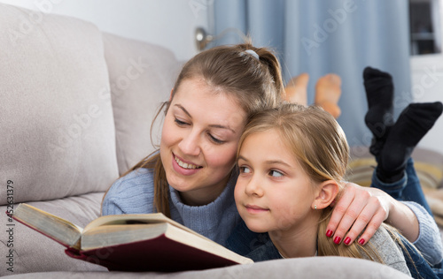 Cheerful pre-teen girl and her mother reading book together at home
