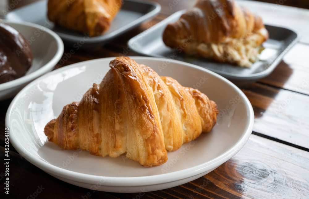 Close up of plain croissants served with plate on wooden table. Croissant is a French buttery, flaky and crescent-shaped bread.