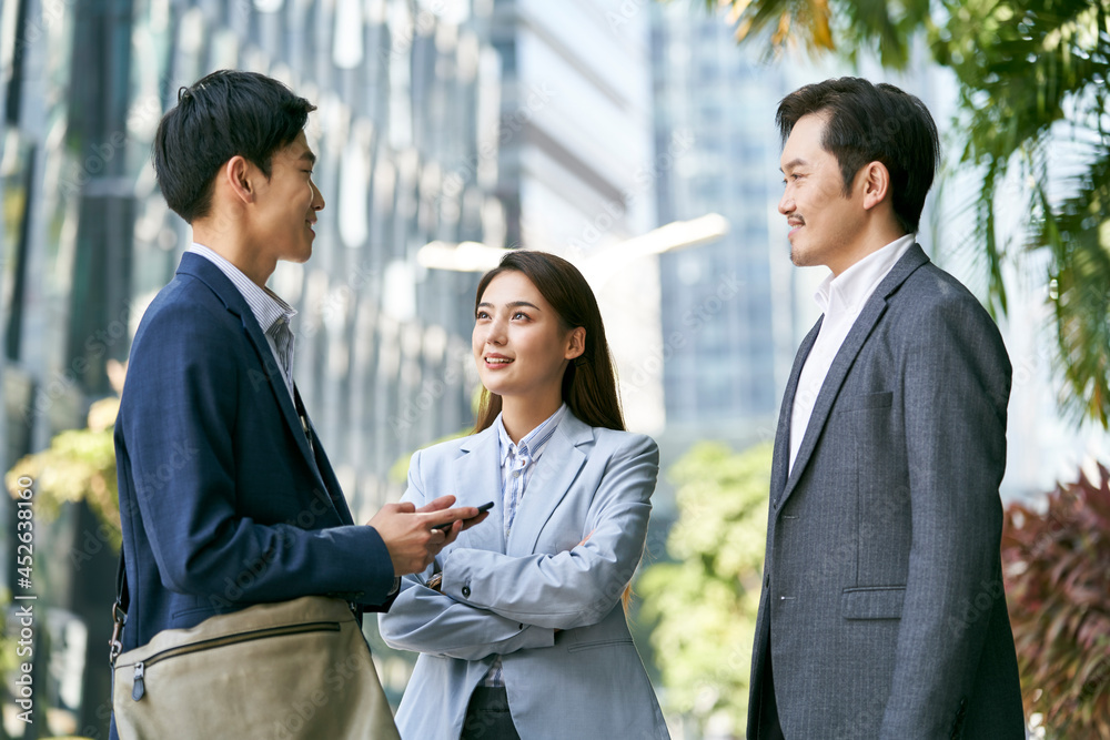 team of three asian business people standing on street talking chatting outdoors in downtown financial district