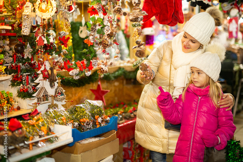 Smiling female and her daughter are choosing decorations for Christmas tree in the market outdoor. High quality photo