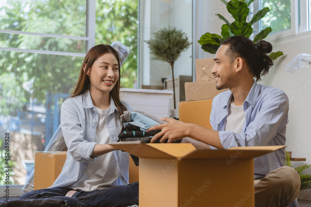 Happy couple asian young woman, man.packing stuff clothes, give second hand for donate, check list object in cardboard box. Moving, preparing in new home, apartment relocation. Mortgage, real estate. Happy couple asian young woman, man.packing stuff clothes, give second hand for donate, check list object in cardboard box. Moving, preparing in new home, apartment relocation. Mortgage, real estate.