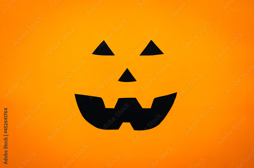 Halloween pumpkin face background from cutting orange and black paper. Minimal halloween concept.