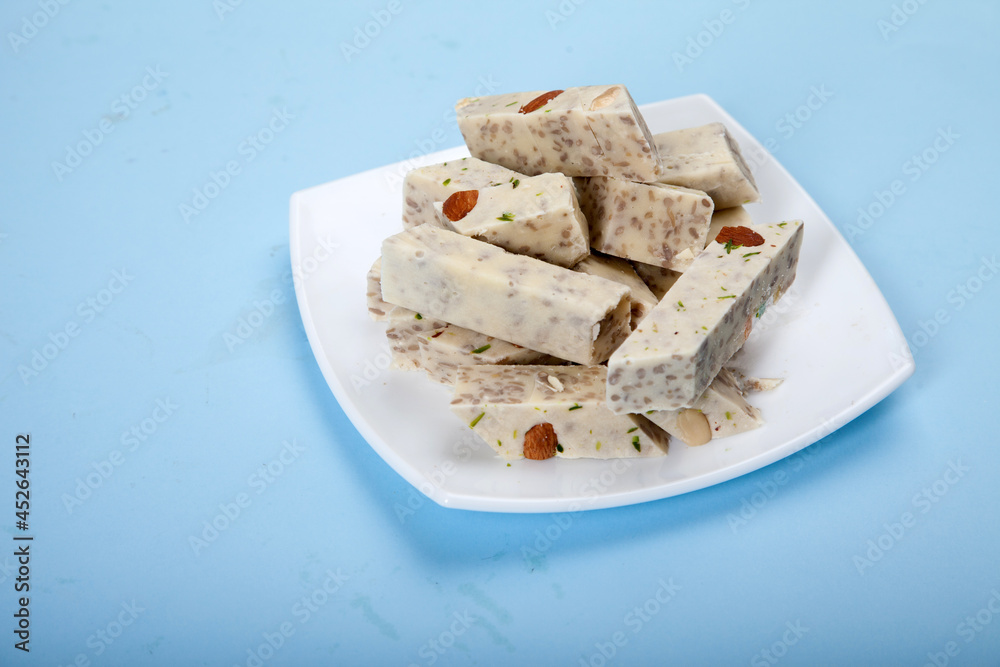 Halva with pistachios and almonds is on a white porcelain plate against a blue background. Halva with pistachios and almonds is on a white porcelain plate against a blue background.