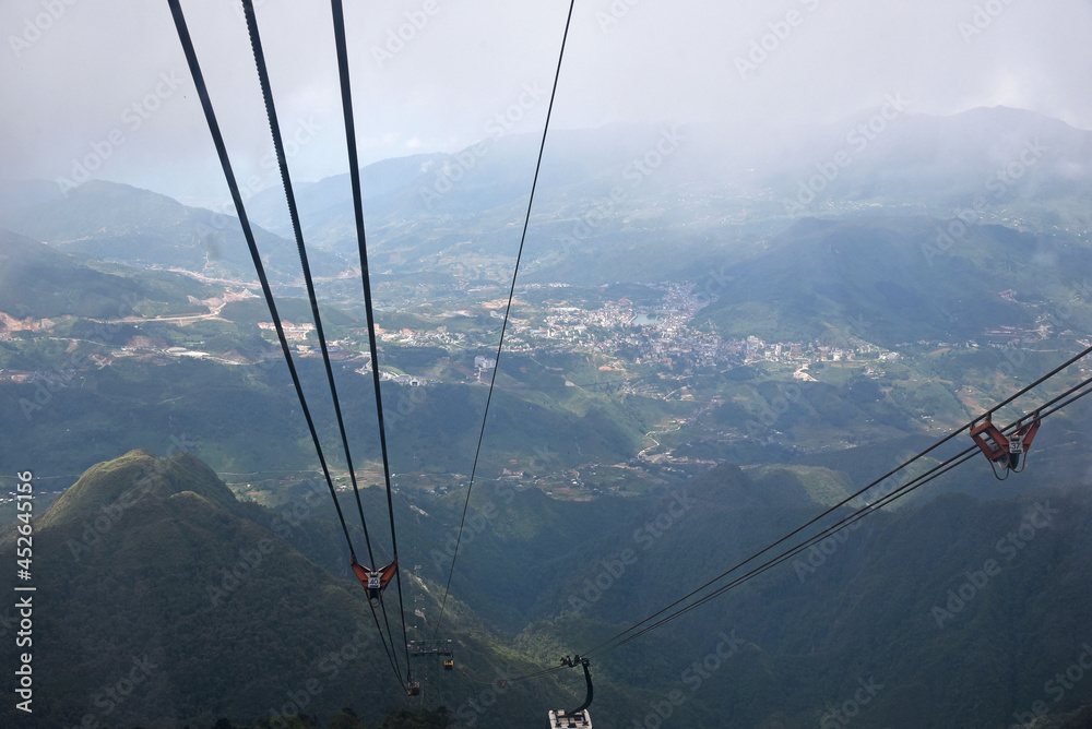View from the cable car cabin to the mountain valley and the city under low clouds, top view