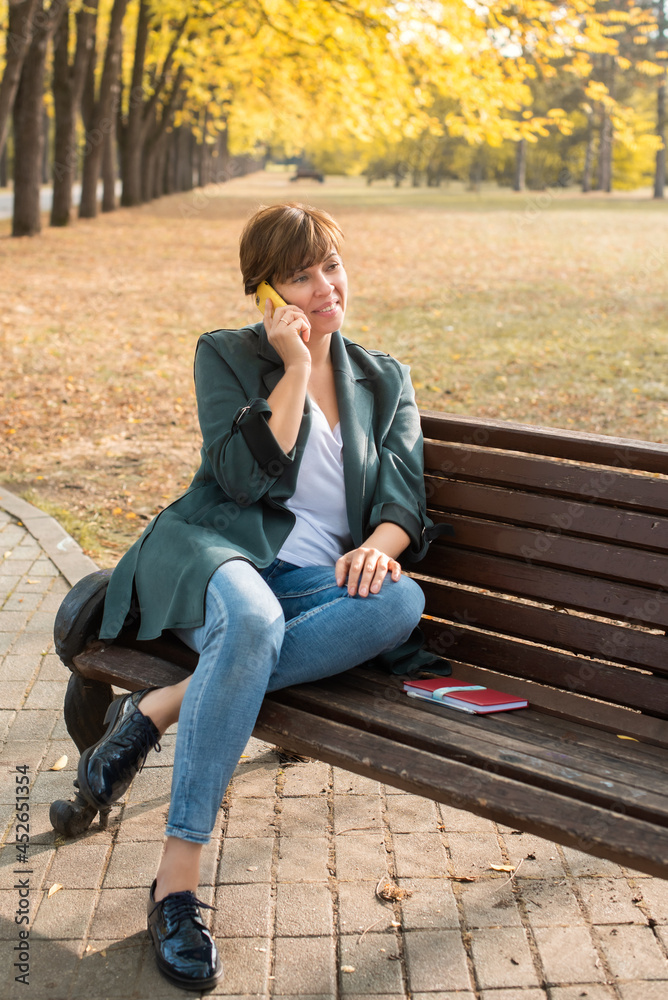 middle-aged woman talking on the phone in autumn park. orange leaves. concepts about senior people middle-aged woman talking on the phone in autumn park. orange leaves. concepts about senior people