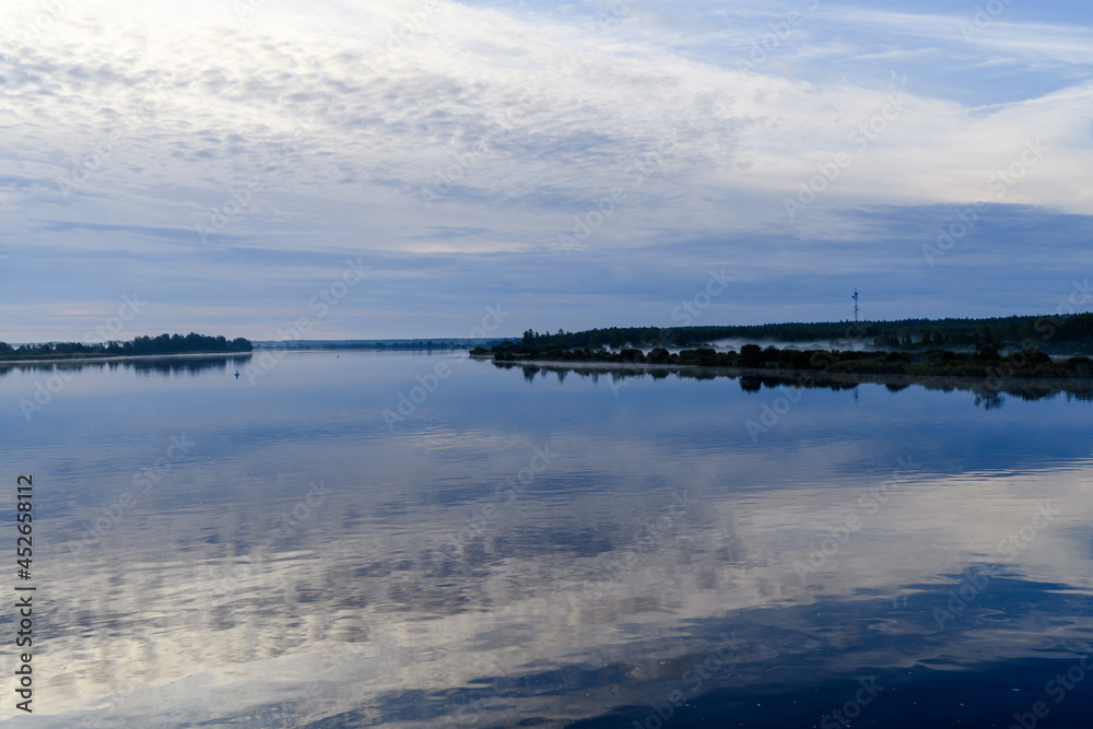 Beautiful, gentle morning landscape during sunrise with atmospheric haze and reflection of clouds in the water. Svir River, Leningrad Region, Russia.
