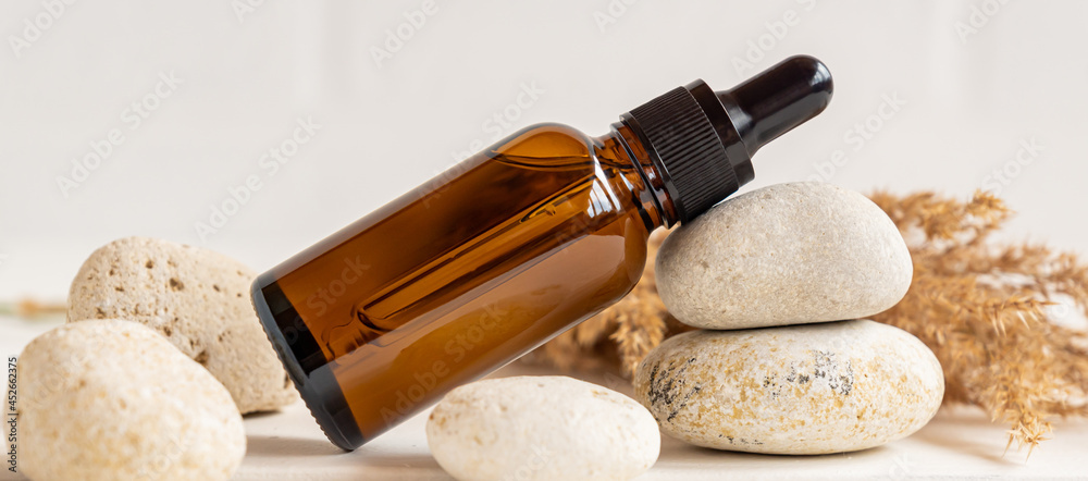 Side view composition with dark glass dropper bottle wit essential oil and stones and dry reeds. home spa and skin care concept - obrazy, fototapety, plakaty 