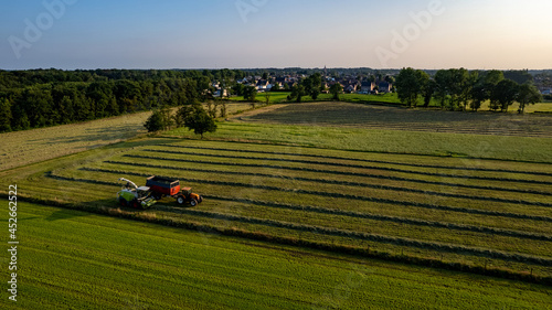 Aerial of tractor baler making straw bales in field after wheat harvest in summer on farm. High quality photo