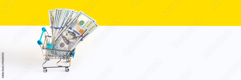 Toy supermarket cart or shopping trolley full of money isolated on yellow and white background. Money loan or sale concept. Long Banner with copy space. Toy supermarket cart or shopping trolley full of money isolated on yellow and white background. Money loan or sale concept. Long Banner with copy space.
