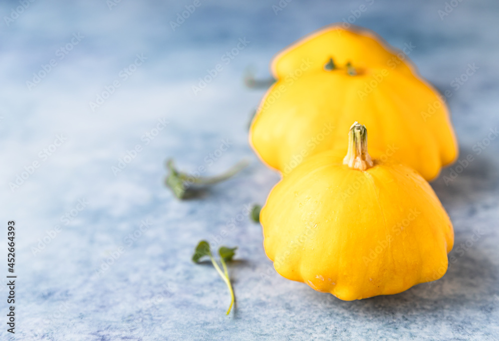 Naklejka premium Fresh ripe yellow patissons, squash or dish-shaped pumpkin on blue concrete background. Harvest of organic garden vegetables.