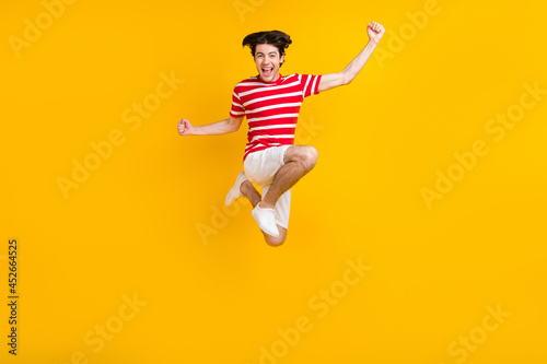 Full size photo of happy cheerful young raise fists jump up good mood winner isolated on yellow color background