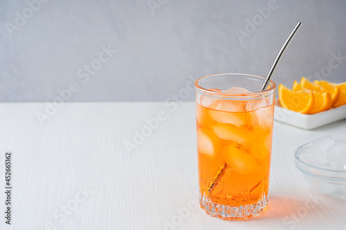 Φωτογραφία Glass of cold refreshing orange carbonated drink served with metal straw, ice cubes and citrus slices on white wooden table at kitchen in hot summer season full of vitamin