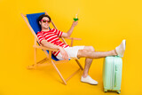 Photo of charming pretty young guy dressed red t-shirt sitting lounge chair drinking cocktail isolated yellow color background