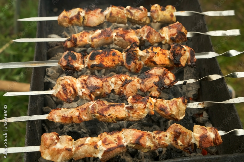 Process of cooking roasted pork meat on skewers on charcoal grill, barbecue, shashlik on nature. Delicious food on metal skewer in bbq. Picnic time, resting outdoors on nature concept. Process of cooking roasted pork meat on skewers on charcoal grill, barbecue, shashlik on nature. Delicious food on metal skewer in bbq. Picnic time, resting outdoors on nature concept.