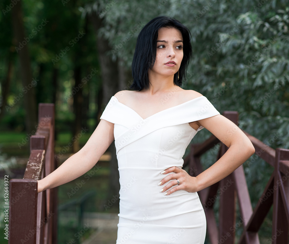 Beautiful, attractive and elegant Caucasian brunette girl posing while standing on the bridge in the park. Fashion concept. Beautiful, attractive and elegant Caucasian brunette girl posing while standing on the bridge in the park. Fashion concept.