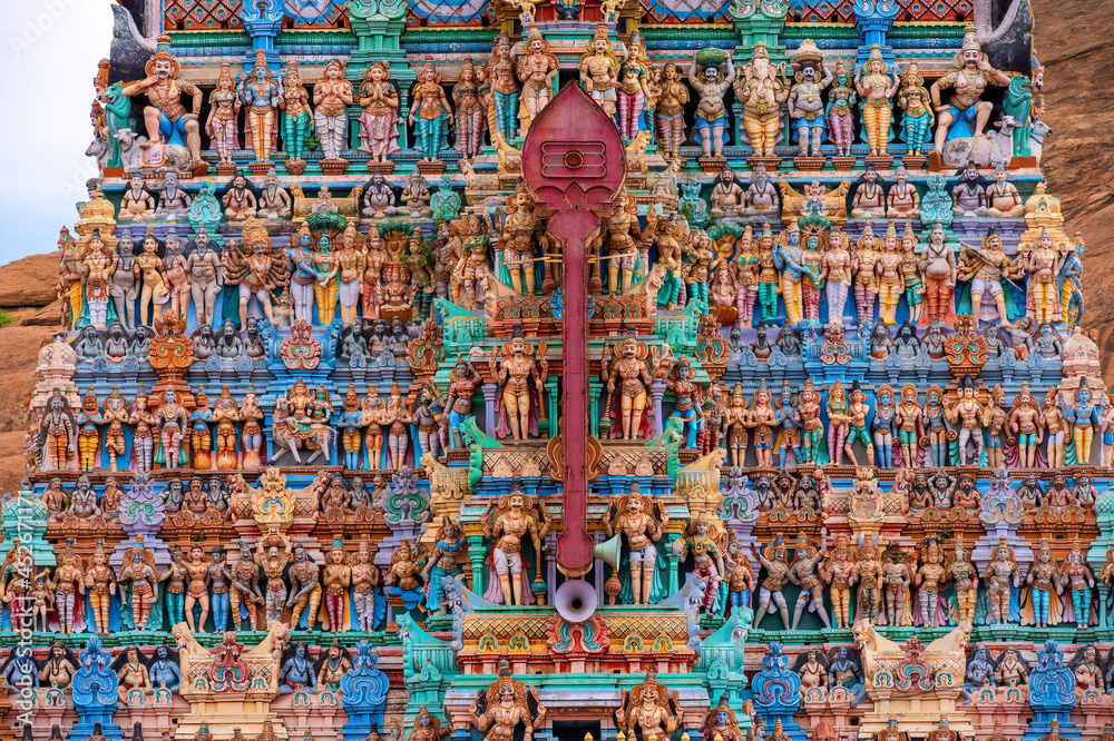 Old south indian temple in close up with full architecture details. Multi colour temple tower in south India surrounded by mountains and rocks..