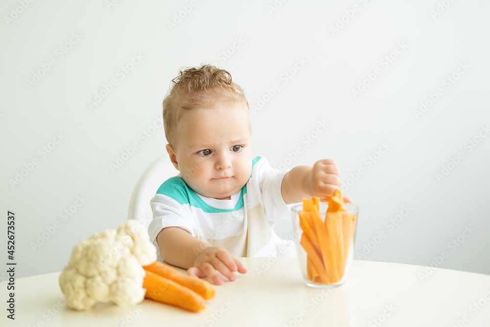 Baby boy sitting in a Childs chair eating carrot slices on white background. Baby boy sitting in a Childs chair eating carrot slices on white background.